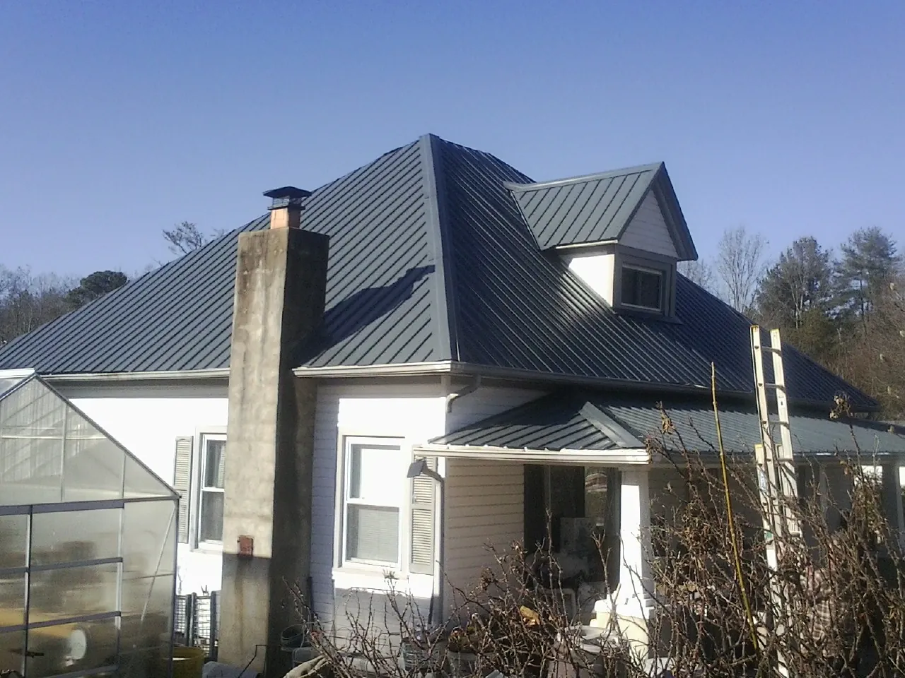 Dark blue standing seam metal roof on a white farmhouse with dormer — Slate & Tile Roof Repair by Roofing Brothers in Poteet