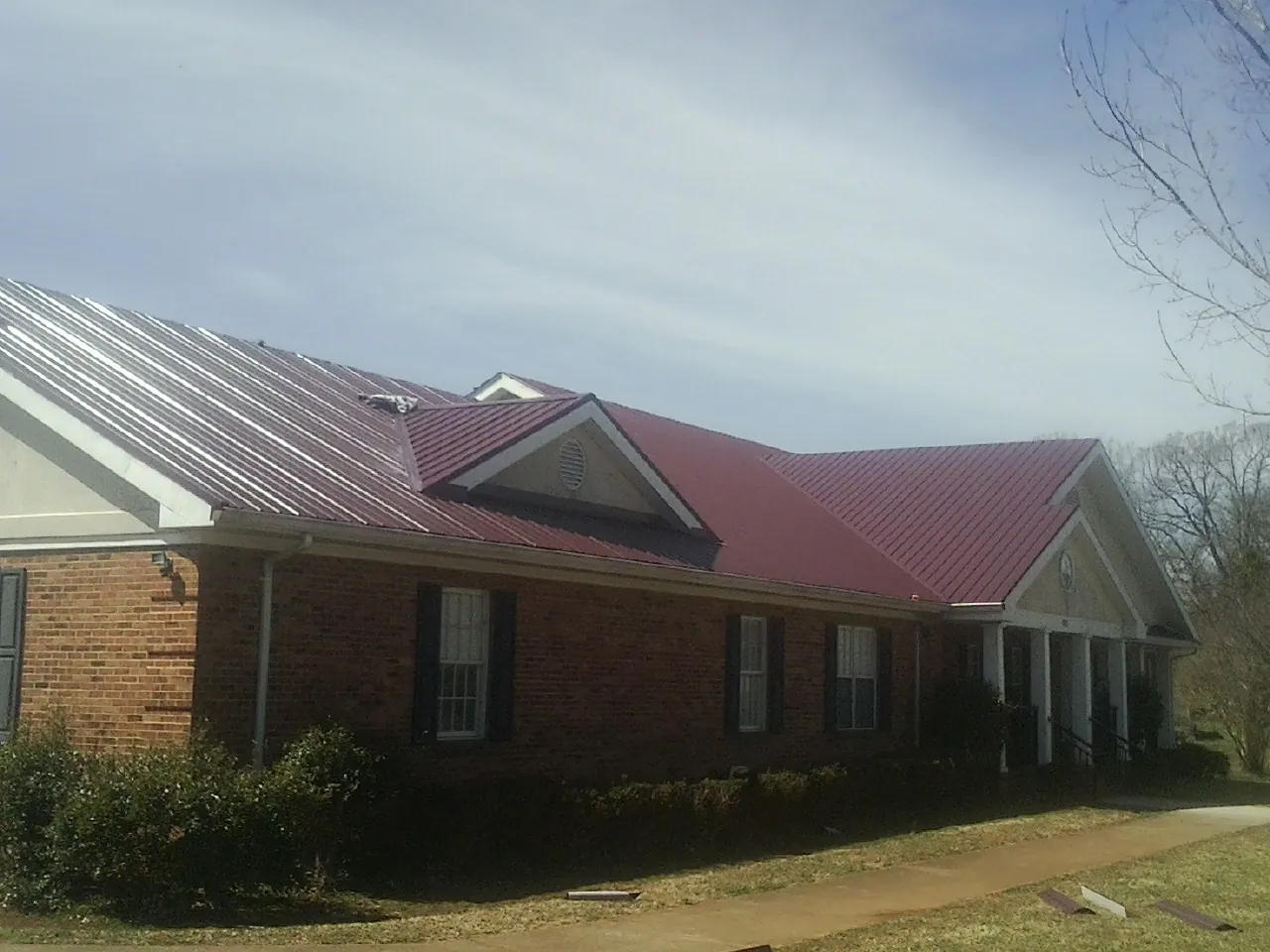 Red metal roof with gabled entries on a long brick building, from a Hail Damage Roof Repair job in Poteet