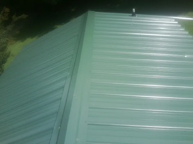 New green metal panels meeting at the ridge of a roof — Flat Roof Repair work by our crew in Poteet