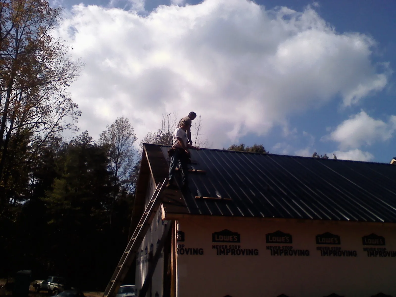 Roofer fastening dark metal panels high against a cloudy sky, from a Roof Inspection job in Poteet